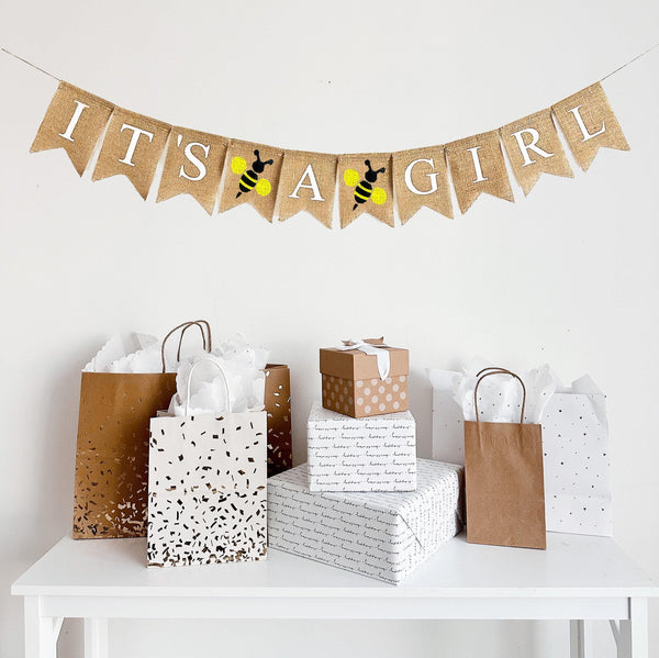 A burlap banner reading it&#39;s a girl with yellow and black bumblebees between the words.