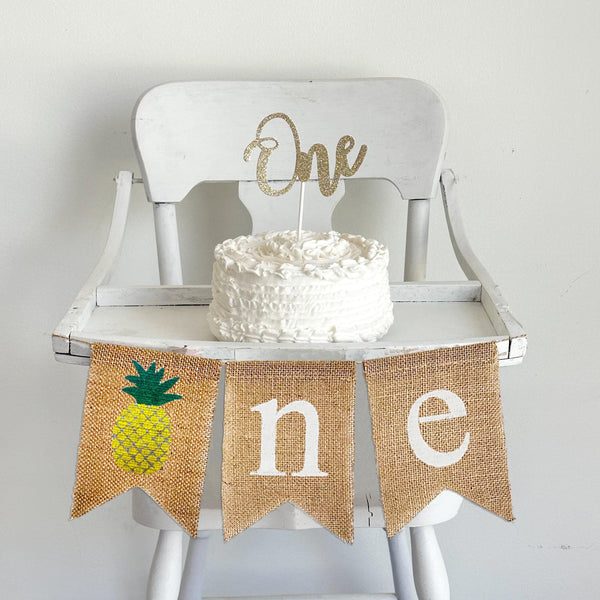 Pineapple first birthday burlap banner. With a pineapple as the O followed by n e in white letters, this high chair banner is perfect for a tropical first birthday party.