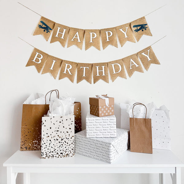 This is a burlap banner made of fishtail shaped flags measuring 4.5 by 6.5 inches each. The top string has the word HAPPY spelled in white letters with an image of a navy vintage plane on either end. The bottom string has the word BIRTHDAY in white.