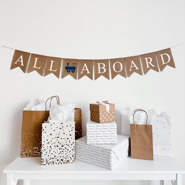 A burlap banner that reads all aboard with a navy train between the words.