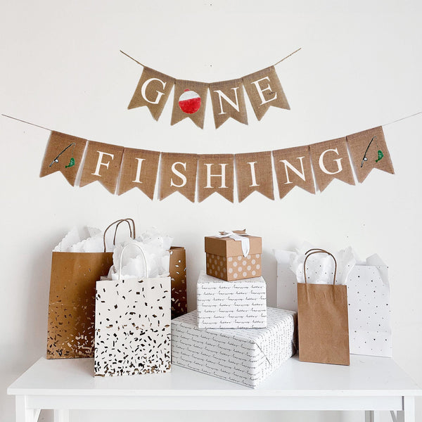 A two tiered burlap banner. The first tier reads gone with a red and white fishing bobber as the o. The second tier reads fishing with an image of a fishing rod with a green fish on it on either side of the word.