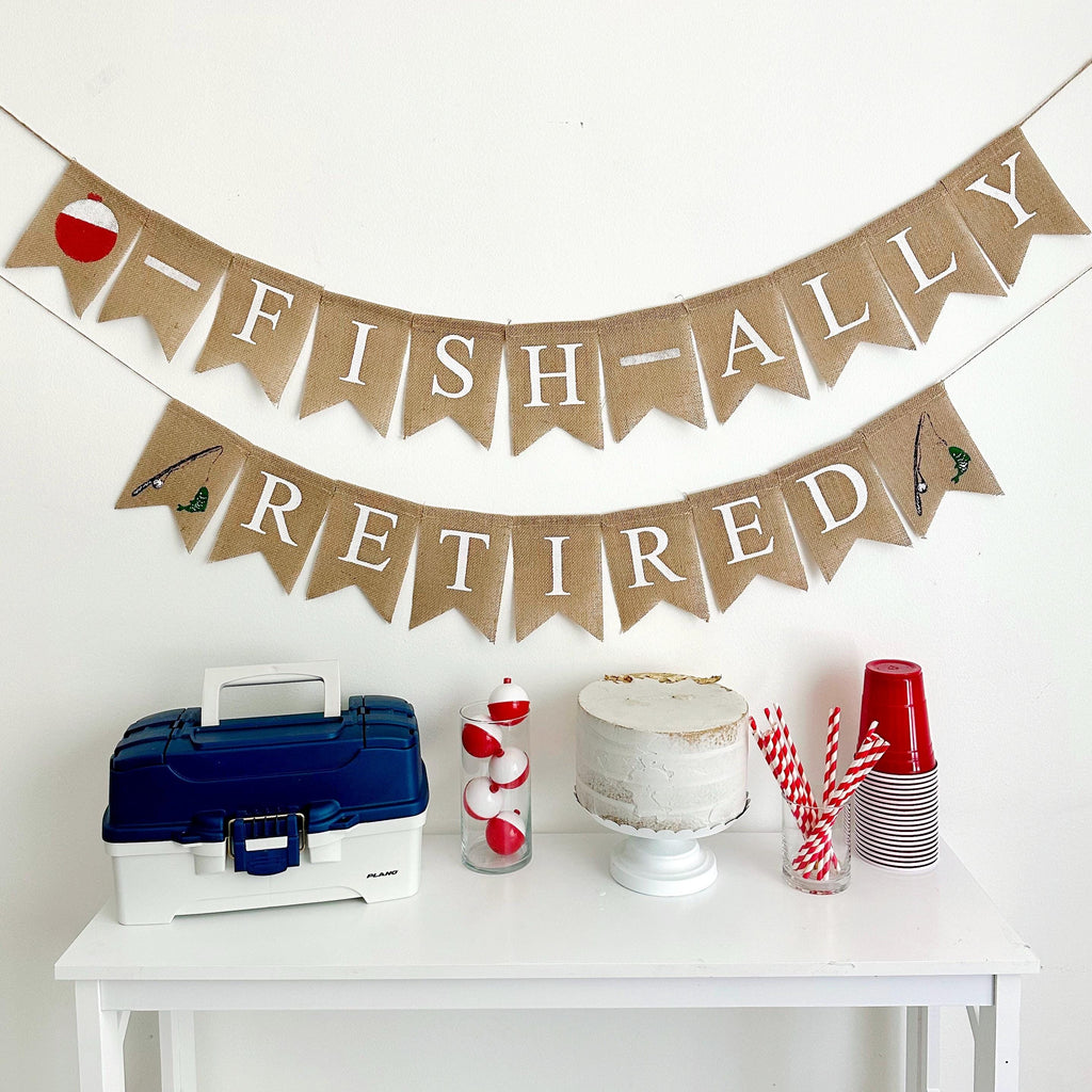 A two tiered burlap banner. The first tier reads ofishally with a red and white fishing bobber as the o. The second tier reads retired with a fishing rod and fish image on either side of the word.