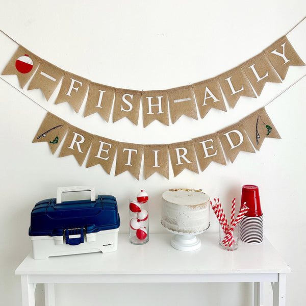 A two tiered burlap banner. The first tier reads ofishally with a red and white fishing bobber as the o. The second tier reads retired with a fishing rod and fish image on either side of the word.