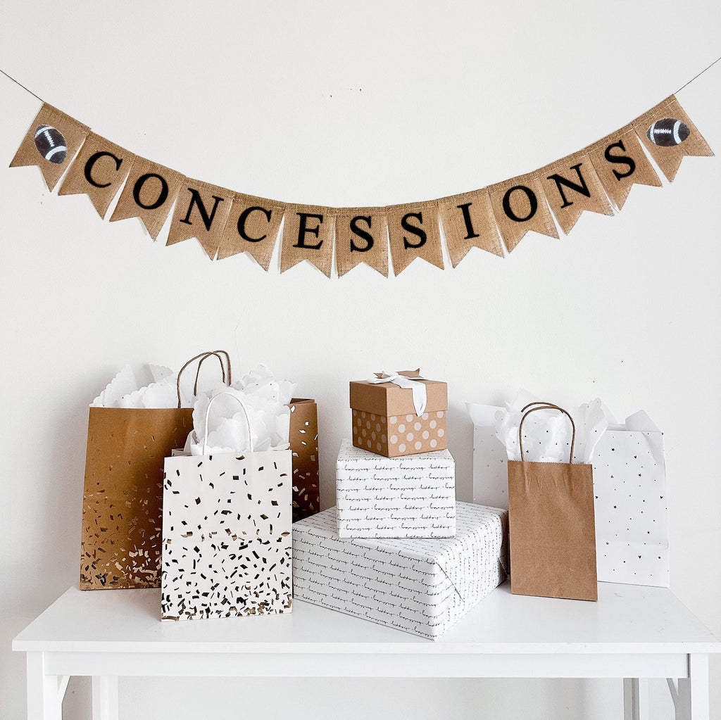 This is a burlap banner made of 4.5 by 6.5 inch fishtail shaped flags. It spells CONCESSIONS in black capital letters and has a hand stenciled image of a football on either end.