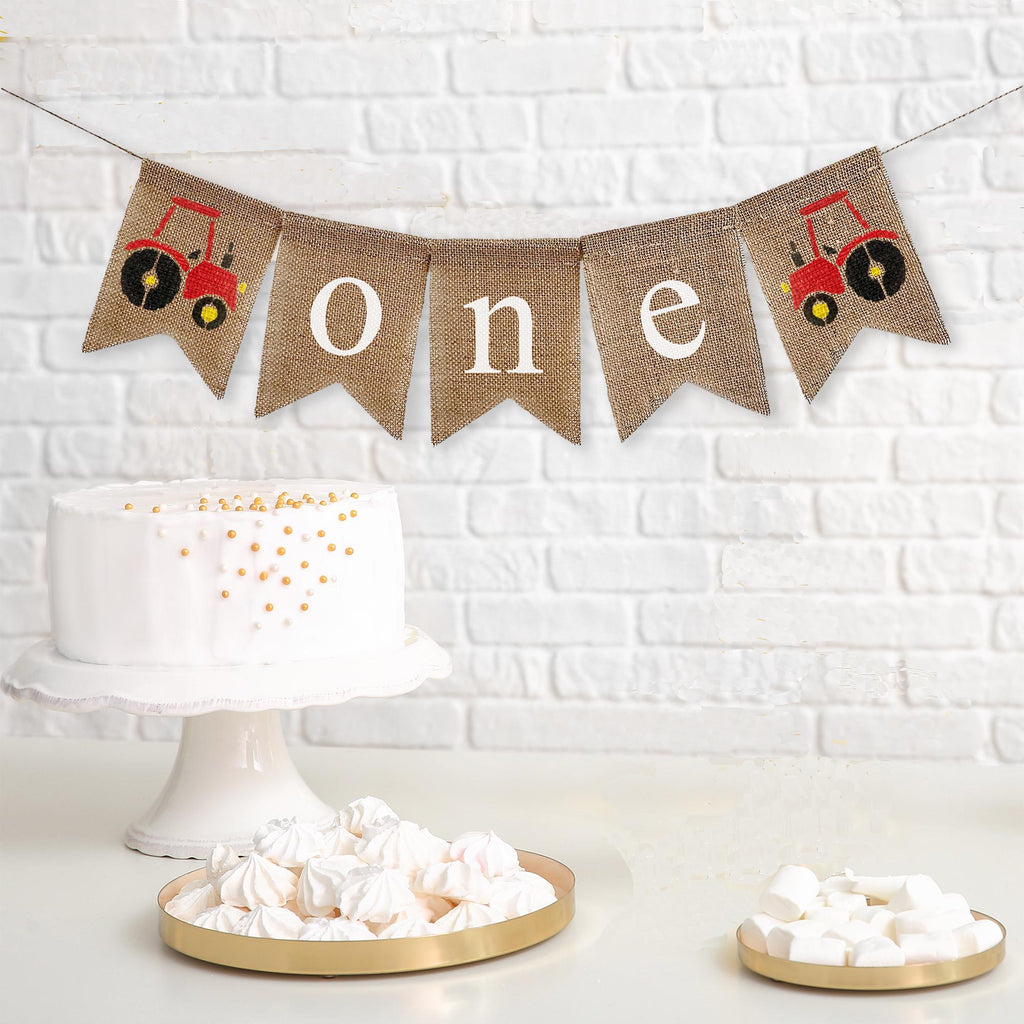 This is a burlap banner made of 4.5 by 6.5 inch fishtail shaped flags. The word ONE is spelled out in white lowercase letters. There is a hand stenciled image of a red tractor on either end.