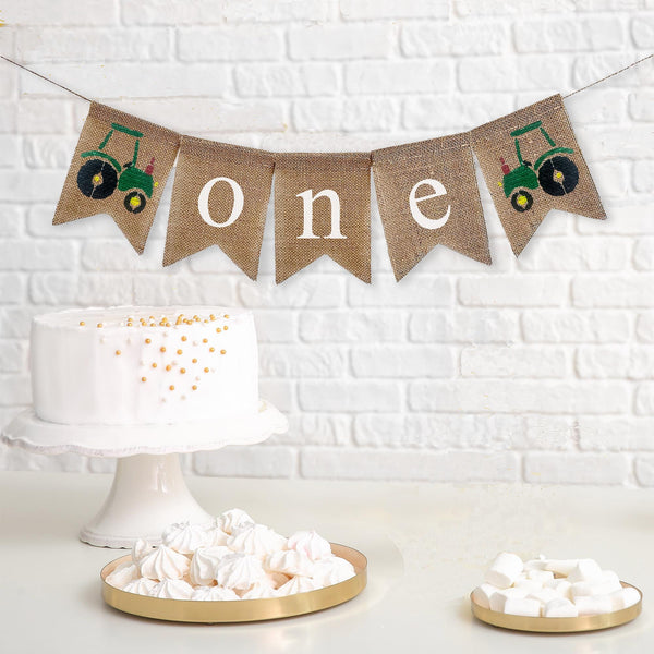 This is a burlap banner made of 4.5 by 6.5 inch fishtail shaped flags. The word ONE is spelled out in white lowercase letters. There is a hand stenciled image of a green tractor on either end.