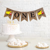 This is a burlap banner made of 4.5 by 6.5 inch fishtail shaped flags. The word ONE is spelled out in black uppercase letters. There is a hand stenciled image of a red and yellow dump truck on either end.