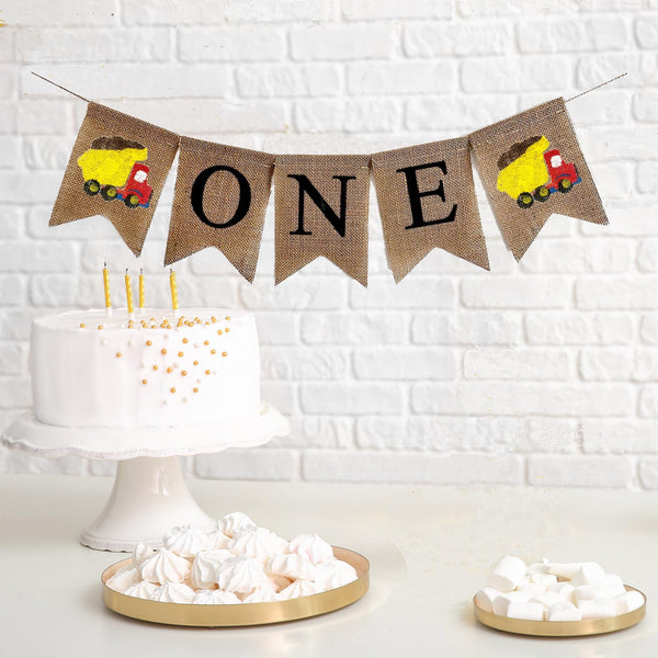 This is a burlap banner made of 4.5 by 6.5 inch fishtail shaped flags. The word ONE is spelled out in black uppercase letters. There is a hand stenciled image of a red and yellow dump truck on either end.