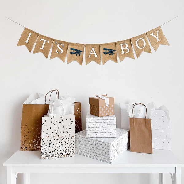 This is a burlap banner made from 4.5 inch by 6.5 inch fishtail shaped flags. IT&#39;S A BOY is spelled out in white capital letters. There is an image of a navy vintage airplane between each of the words. There is a total of two images.