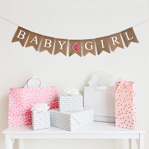 A burlap banner that reads baby girl with a pink & green watermelon between the words.