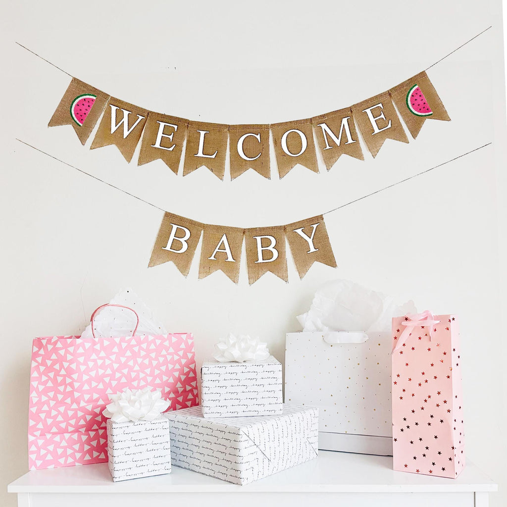 A two tiered burlap banner. The first tier reads welcome with pink & green watermelon images on each end. The second tier reads baby.