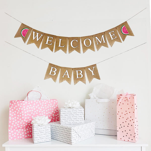 A two tiered burlap banner. The first tier reads welcome with pink & green watermelon images on each end. The second tier reads baby.