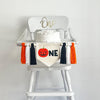 A banner made with a 5 x 7 canvas center flag with an orange Jack O Lantern followed by black letters N E. On either side of the banner there are 3 tassels in this order, black, white, orange for a total of 6 tassels with wooden beads in between each