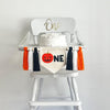A banner made with a 5 x 7 canvas center flag with an orange Jack O Lantern followed by black letters N E. On either side of the banner there are 3 tassels in this order, black, white, orange for a total of 6 tassels with wooden beads in between each