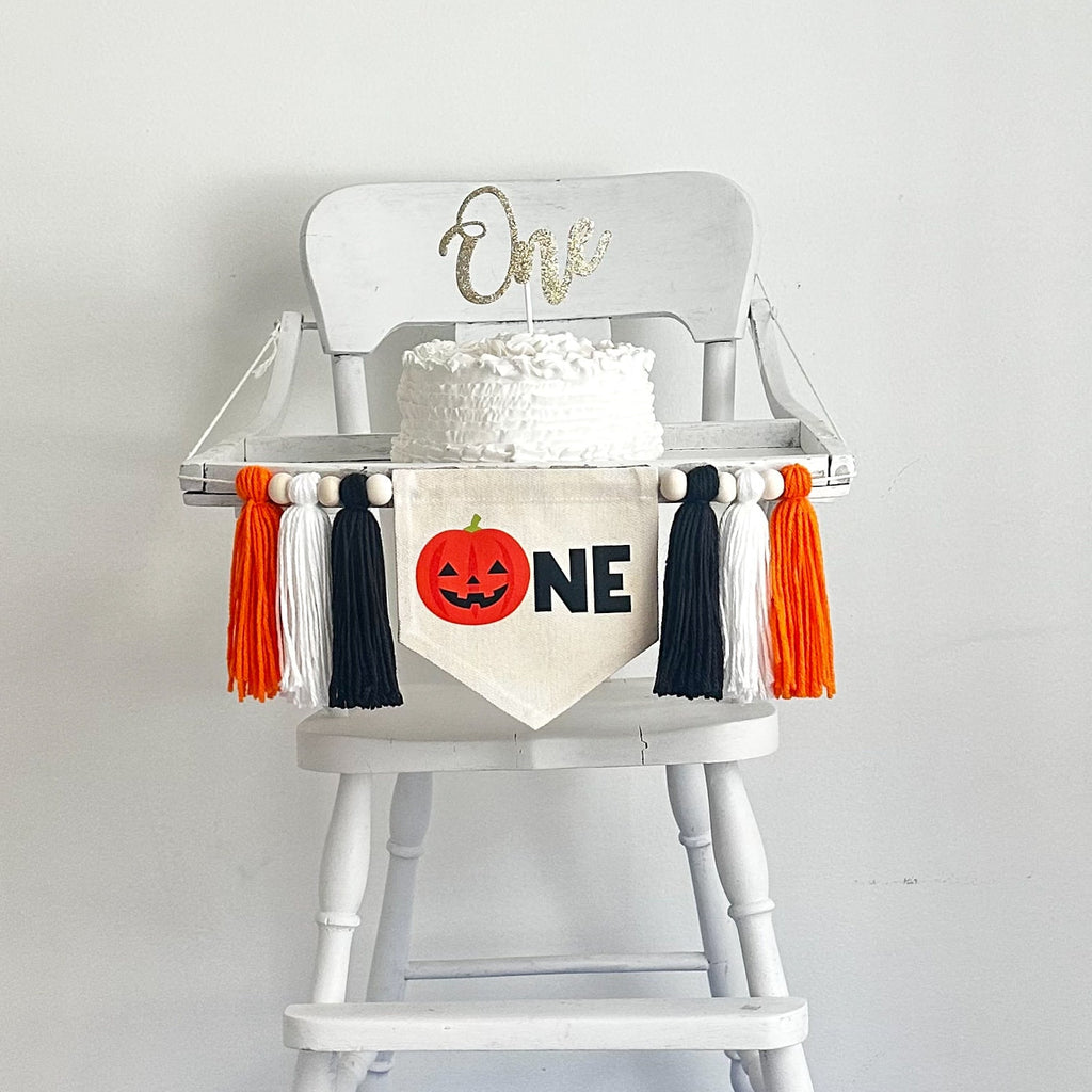 A banner made with a 5 x 7 canvas center flag with an orange Jack O Lantern followed by black letters N E. On either side of the banner there are 3 tassels in this order, black, white, orange for a total of 6 tassels with wooden beads in between each