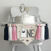 A 5 x 7 inch canvas center flag with a ghost followed by the letters NE in black and accented with a spider, bats and the word BOO in pink. On each side there is a light pink, white and black 5 inch yarn tassel, each separated by a wooden bead.