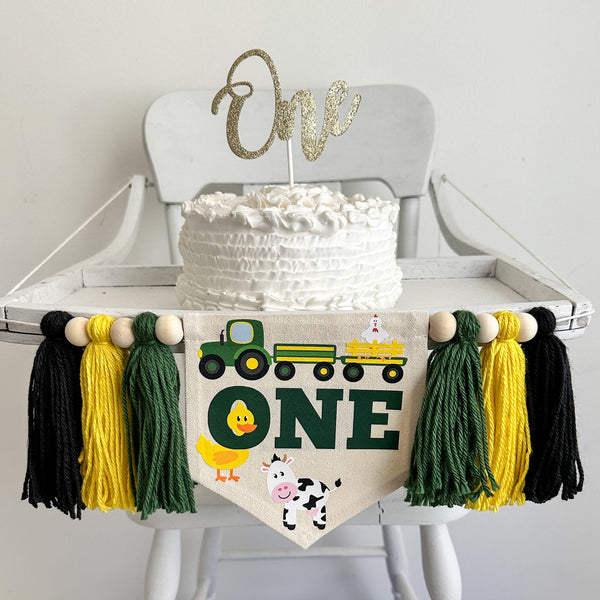 A 5 x 7 inch canvas center flag with the word ONE in green letters. There is a tractor above ONE pulling a hay wagon with a chicken in it. There is also a duck and a cow. On each side is a green, yellow and black tassel separated by wooden beads.