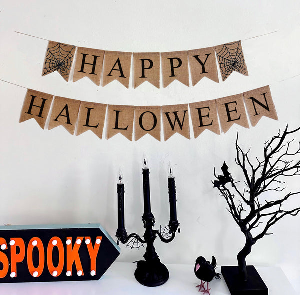 A two tiered banner. The first tier reads happy and features spiderweb patterns on either side of the word. The second tier reads Halloween.