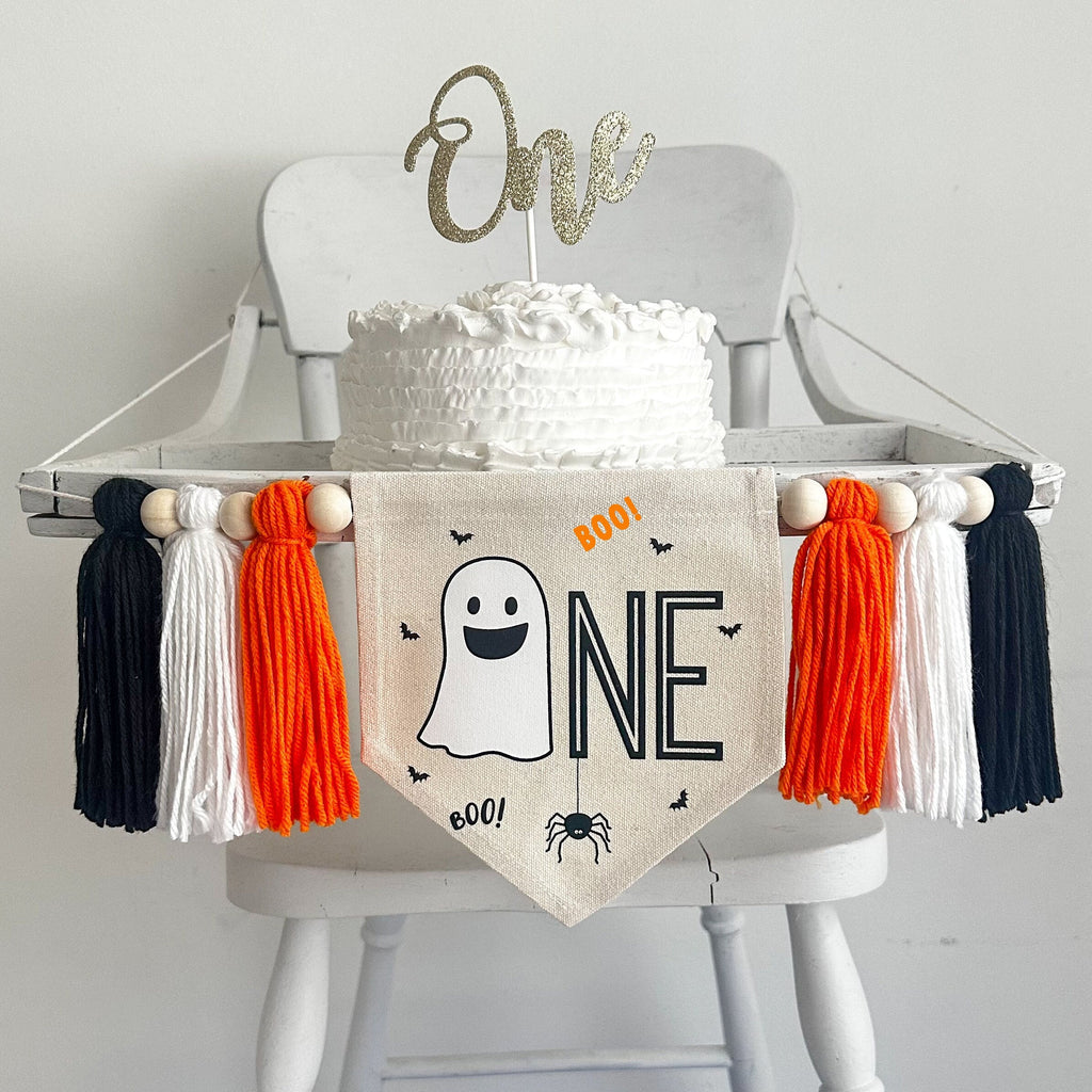 A 5 by 7 inch canvas center flag with a ghost followed by the letters NE in black, accented with a spider, bats and the word BOO. There is an orange, white and black yarn tassel on each side, all separated by wooden beads.