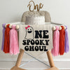 A 5 x 7 inch canvas center flag with a ghost with a pink bow followed by the letters NE in black and the word SPOOKY GHOUL underneath. On each side there is a pink, dark orange and lavender 5 inch yarn tassel, each separated by a wooden bead.