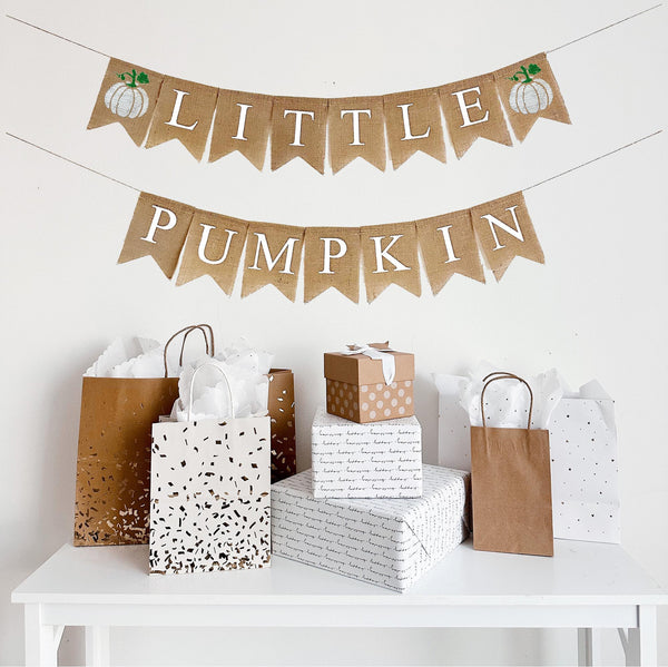 Burlap banner featuring two white hand stenciled pumpkins with green stem. Letter flags spell out the words Little Pumpkin in white letters.