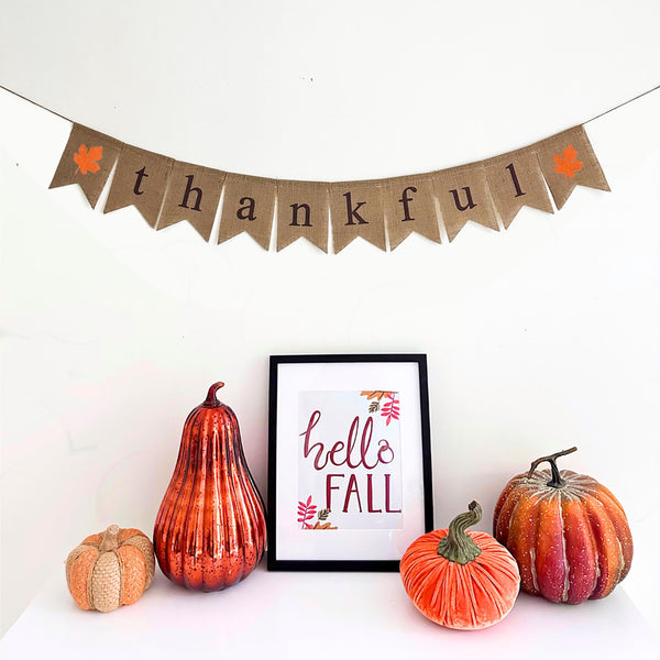 Thankful banner with brown lowercase letters and an orange maple leaf on both ends of the word. Each letter or image is printed on a fishtail burlap flag.