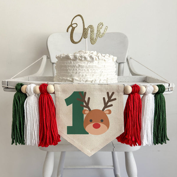 A 5 x 7 canvas center flag with a big green number 1 with a cute reindeer head beside it to the right. There is a red, white and dark green 5 inch yarn tassel on each side, each separated by a wooden bead for a total of 6 tassels and 6 beads.