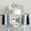 A 5 x 7 inch canvas center flag with a ghost followed by the letters NE in black and accented with a spider, bats and the word BOO in light blue. On each side there is a light blue, white and black 5 inch yarn tassel, each separated by a wooden bead.