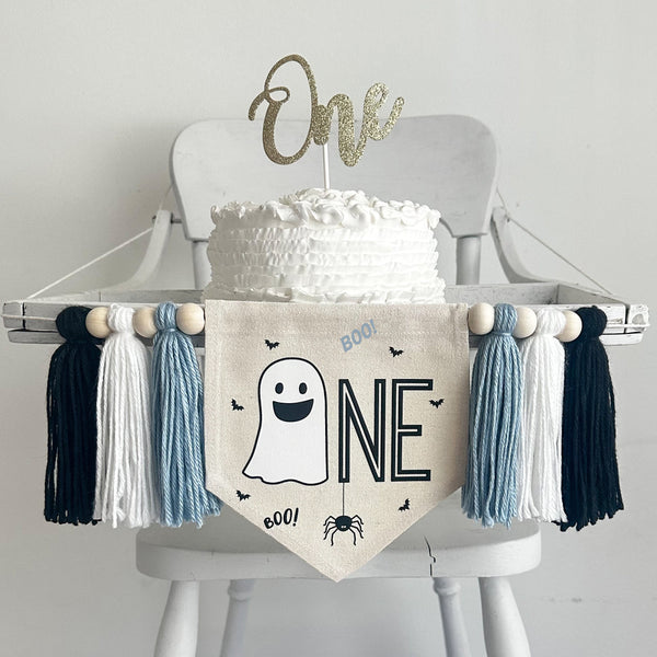 A 5 x 7 inch canvas center flag with a ghost followed by the letters NE in black and accented with a spider, bats and the word BOO in light blue. On each side there is a light blue, white and black 5 inch yarn tassel, each separated by a wooden bead.