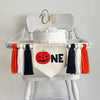 A 5 x 7 inch canvas center flag with an orange Jack O Lantern followed by the letters NE in black to spell the word ONE. On each side there is a black, white and orange 5 inch yarn tassel, each separated by a wooden bead.