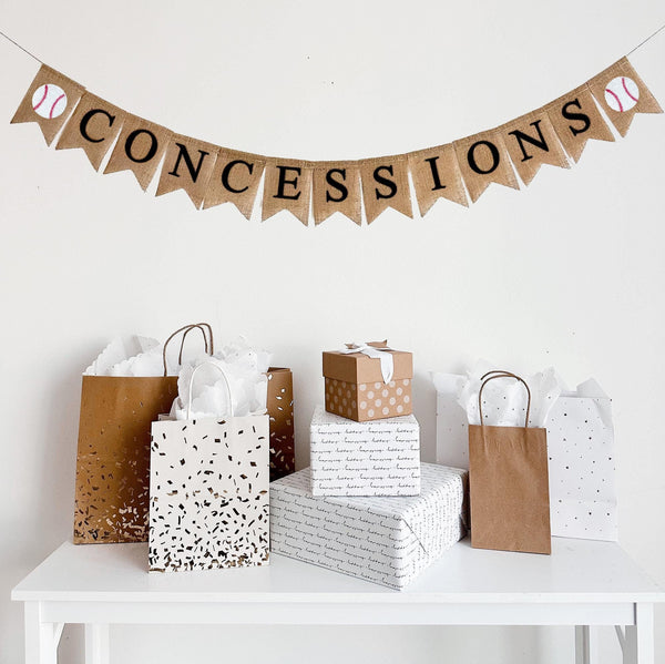 A burlap banner made from 4.5 by 6.5 inch fishtail shaped flags. The banner spells the word CONCESSIONS in black capital letters. On each end, there is an image of a hand stenciled baseball.