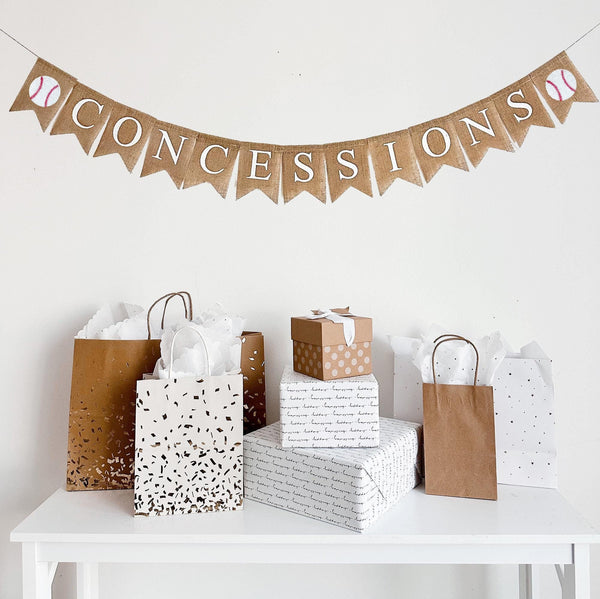 A burlap banner made from 4.5 by 6.5 inch fishtail shaped flags. The flags spell out the word CONCESSIONS in white capital letters and there is an image of a hand stenciled baseball on each end.