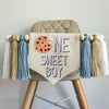 A 5 by 7 center flag with a chocolate chip cookie followed by the letters NE in light blue and SWEET BOY in light blue. On each side there are 5 inch light blue, tan and white tassels each separated by a wooden bead for a total of 6 tassels.