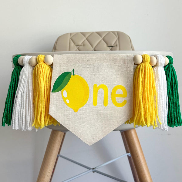 A 5 by 7 inch canvas center flag with a yellow lemon with green leaves as the O, followed by the letters NE in yellow. There is a 5 inch yellow, white and green yarn tassel on each side, each separated by a wooden bead for a total of 6 tassels.
