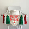 A 6 by 7 inch canvas center flag with the words HALFWAY TO ONE in red with a peppermint as the O. There are 2 criss crossed candy canes under the words. There is a 5 inch green, white and red yarn tassel on each side each separated by a wooden bead.