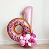 Donut ONE balloon tower with a 34 inch pink number one balloon, 36 inch pink sprinkle donut balloon with a bite taken out of it, on top of a pink latex balloon tower with dark pink, light pink and marble pink.