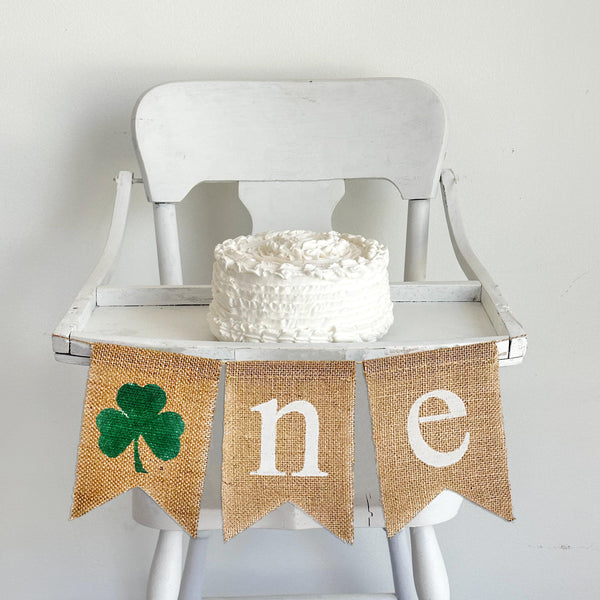 Shamrock first birthday high chair banner. This burlap banner spells out ONE with a green hand stenciled shamrock as the O followed by a flag with a white n and e.