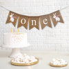 A bunny themed one banner on burlap fishtail flags. This banner starts with one white hand stenciled bunny wearing a pink bow followed by the words one in white lower case letters and ends with another white hand stenciled bunny image wearing a pink bow.