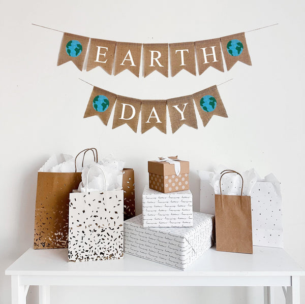A burlap banner made from 4.5 by 6.5 inch fishtail shaped flags. The top line says EARTH in white capital letters with a hand painted image of a blue and green earth on each end. The bottom line says DAY in white capital letters with a hand painted image of a blue and green earth on each end. It comes with   two 110 inch pieces of jute string for stringing.