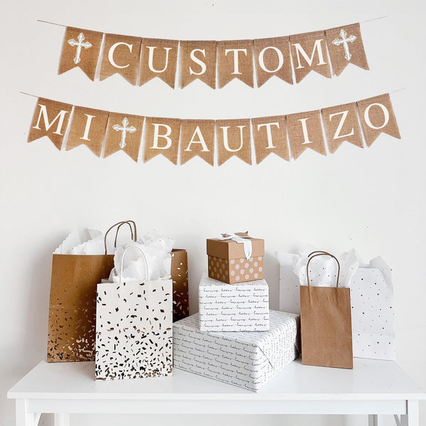 This custom Mi Bautizo banner comes on two lines. The top line is customizable with a white cross on either end of your custom wording. The second line reads Mi Bautizo with a cross between the two words.