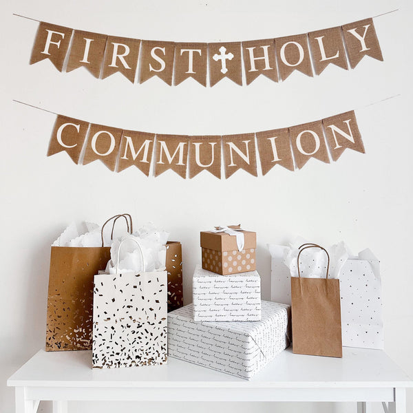 First Holy Communion burlap banner. The first line reads First Holy with a white cross in the middle of the two words, second line reads Communion. The banner is made of burlap with white lettering and the hand stenciled cross add the perfect touch to make this banner perfect for your special celebration.