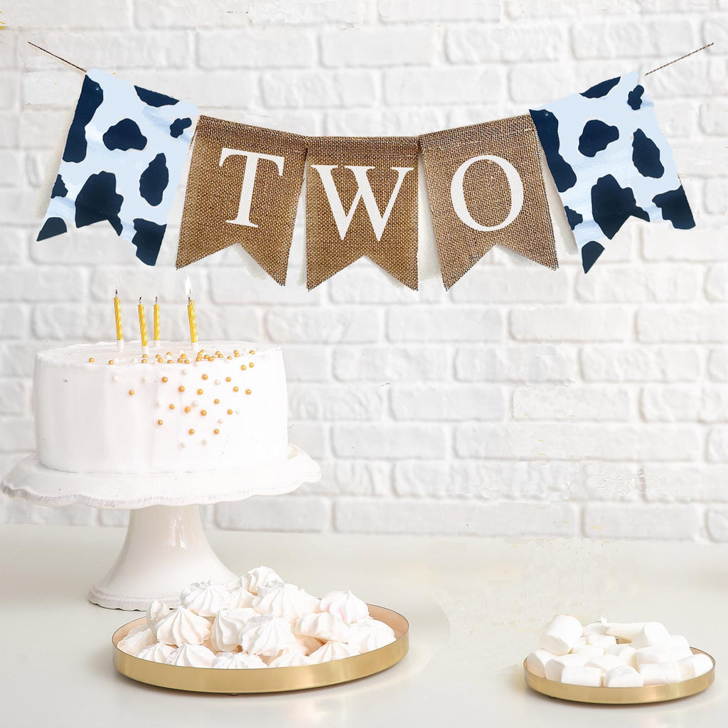 Cow print two banner features two cow print flags on either side of flags spelling out the word TWO. Perfect for a second birthday.