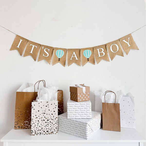 A burlap banner that reads IT&#39;S A BOY with mint and white striped hot air balloons between the words.