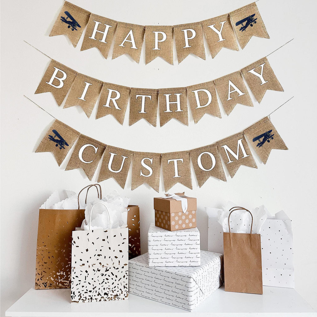 This is a burlap banner made of fishtail shaped flags measuring 4.5 by 6.5 inches each. The top string has the word HAPPY spelled in white letters with an image of a navy vintage plane on either end. The bottom string has the word BIRTHDAY in white. Add a custom name, date or phrase to personalize your event.