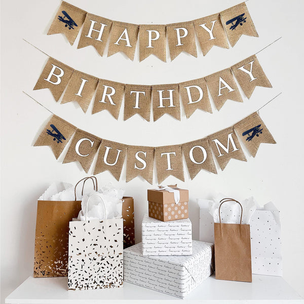 This is a burlap banner made of fishtail shaped flags measuring 4.5 by 6.5 inches each. The top string has the word HAPPY spelled in white letters with an image of a navy vintage plane on either end. The bottom string has the word BIRTHDAY in white. Add a custom name, date or phrase to personalize your event.
