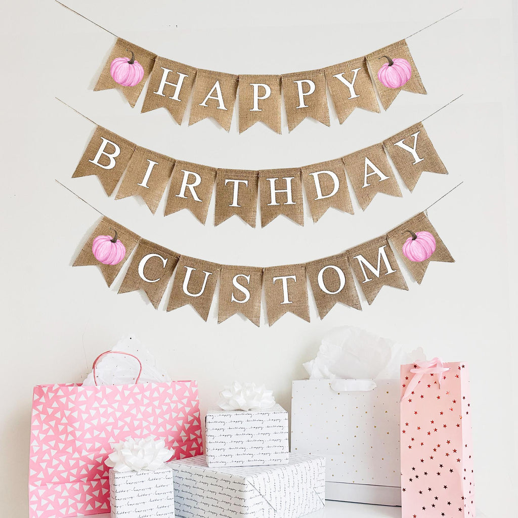 A burlap banner made from 4.5 by 6.5 inch fishtail flags. The top string says HAPPY in white letters, the middle string says BIRTHDAY and the third string is custom letters of your choice. 4 total pink pumpkins are included on the 1st and 3rd string.
