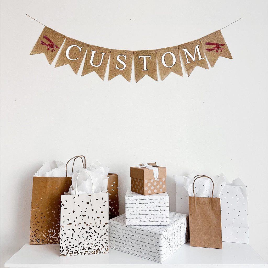 Customizable burlap banner. This banner contains fishtail burlap flags with white lettering,ready to be personalized with a name, date or wording of your choice to customize your special event. On either end of your custom wording, you have the choice of a red hand stenciled vintage airplane or a blue hand stenciled vintage airplane.