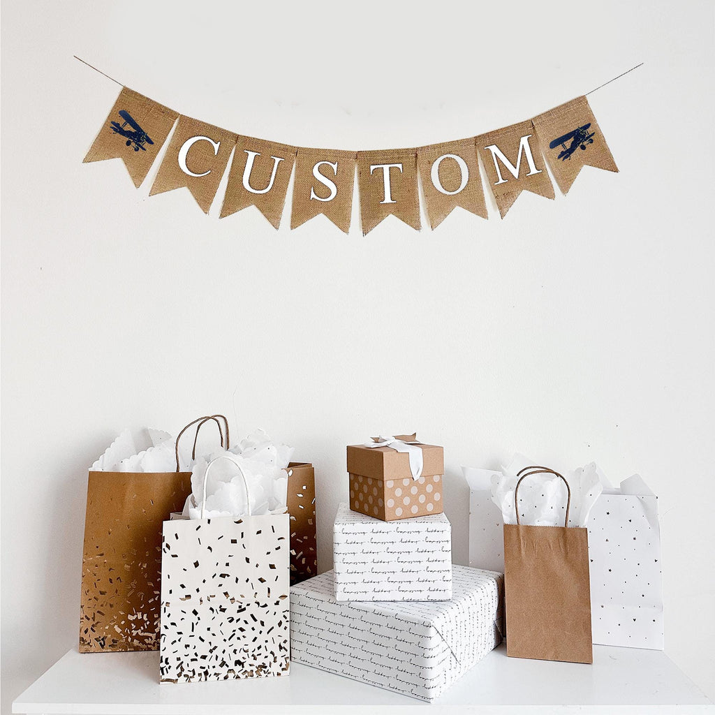 Customizable burlap banner. This banner contains fishtail burlap flags with white lettering,ready to be personalized with a name, date or wording of your choice to customize your special event. On either end of your custom wording, you have the choice of a red hand stenciled vintage airplane or a blue hand stenciled vintage airplane.