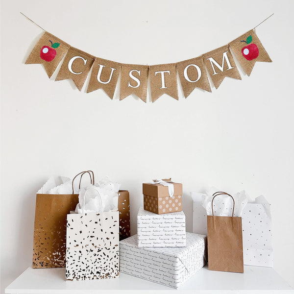 This customizable fruit banner consists of white lettering on a fishtail burlap banner. Add a custom name, date, phrase or wording to make your event extra special. On each end of your custom wording, there is a hand stenciled red apple.
