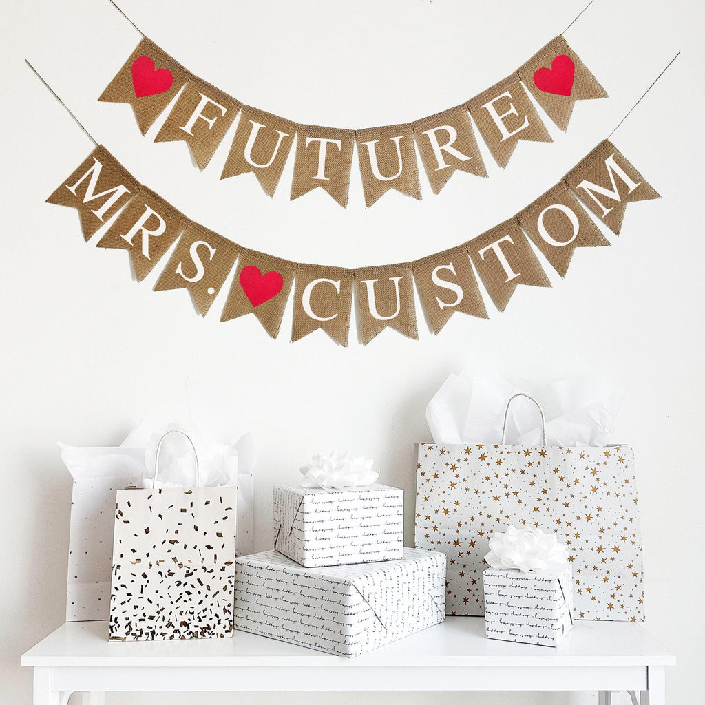 Customize this Future Mrs. Banner with the bride to be&#39;s new last name! The top layer spells out the word Future in white letters with a red heart on either side. The bottom layer spells out the word Mrs. followed by a red heart and then an option to personalize this banner with the bride&#39;s new last name.